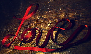 red ribbon making LOVE text on brown wooden surface HD wallpaper