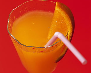 orange juice on clear drinking glass with white straw