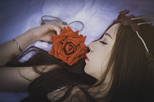 tilt lens photography of brown haired female holding  orange artificial flower
