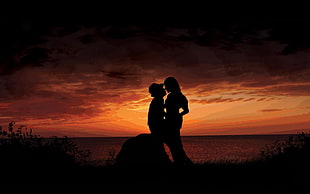 silhouette photo of man and woman near body of water