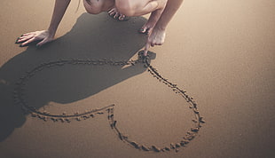photo of person sketching heart on sand during day time