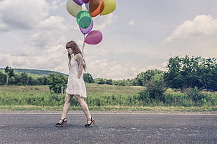 woman in white sleeveless dress while holding balloons