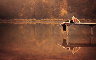 woman lying on gray wooden dock near lake during golden hour HD wallpaper
