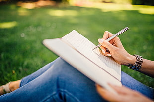 woman in blue jeans and holding pen writing on organizer