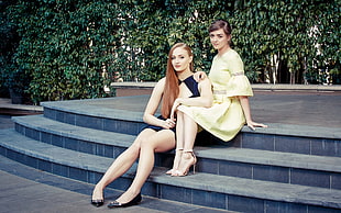two women wearing dresses sitting on a staircase