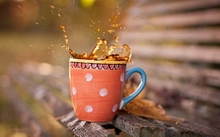 macro shot photography of brown liquid splashing in orange ceramic mug