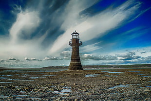brown concrete lighthouse on brown sand under cloudy sky during daytime