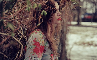 woman wearing white and red floral top leaning on grass wall