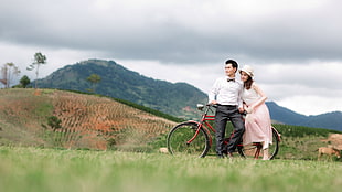 man wearing white dress shirt beside a girl wearing pink dress sitting on red city bicycle during day time