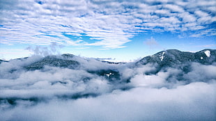 aerial photography of black mountains surrounded by clouds under white citrus clouds