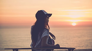 woman wearing white shirt and hat near ocean during golden hour