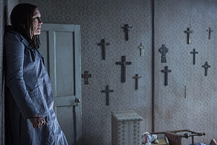 woman in blue long-sleeved top holding rosary near wall with cross in room