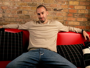 man wearing gray sweater sits on red and black sofa