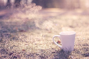 selective focus photography of placed white ceramic mug on grass with smoke steam