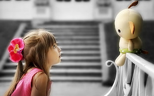 girl in pink dress looking and white doll on white steel rail