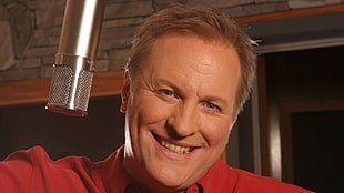 smiling man wearing red top near gray microphone