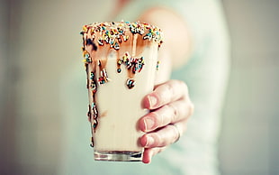 person holding highball glass with ice cream in shallow focus photography
