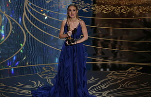 woman wearing blue tank dress holding trophy standing on stage