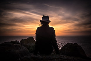silhouette of person wearing bucket hat near body of water during sunset