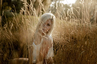 woman in white top sitting on grasses during daytime