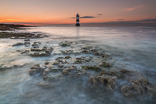 Lighthouse on body of water surrounded stones, penmon