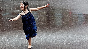 girl wearing blue spaghetti-strap midi dress dancing on the road filled with rain drops