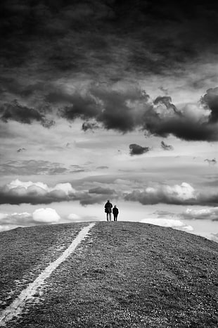 grayscale photography of man and child standing front of clouds on mountain HD wallpaper