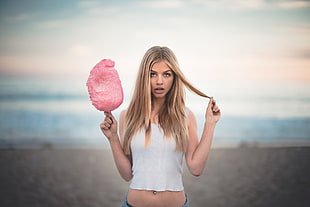 woman in white tank top holding cotton candy while standing on beach