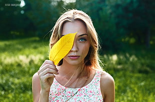 woman holding yellow leaf near green grass field during daytime