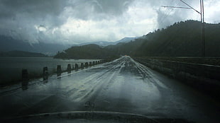 concrete road near body of water and moutain