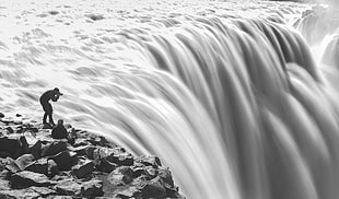grayscale of man holding camera taking picture of falls