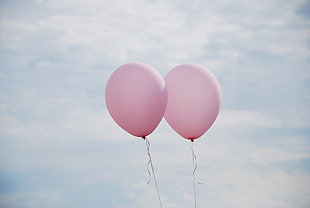 two pink balloons under white clouds during daytime