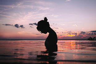 silhouette of a woman in body of water during sunset