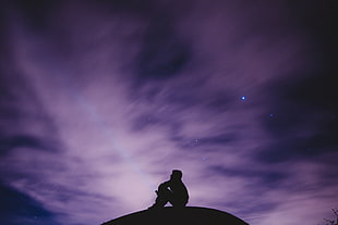 silhouette of person sitting under cloudy sky during nighttime HD wallpaper