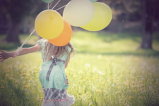 girl holding balloons running on bed of yellow petaled flowers