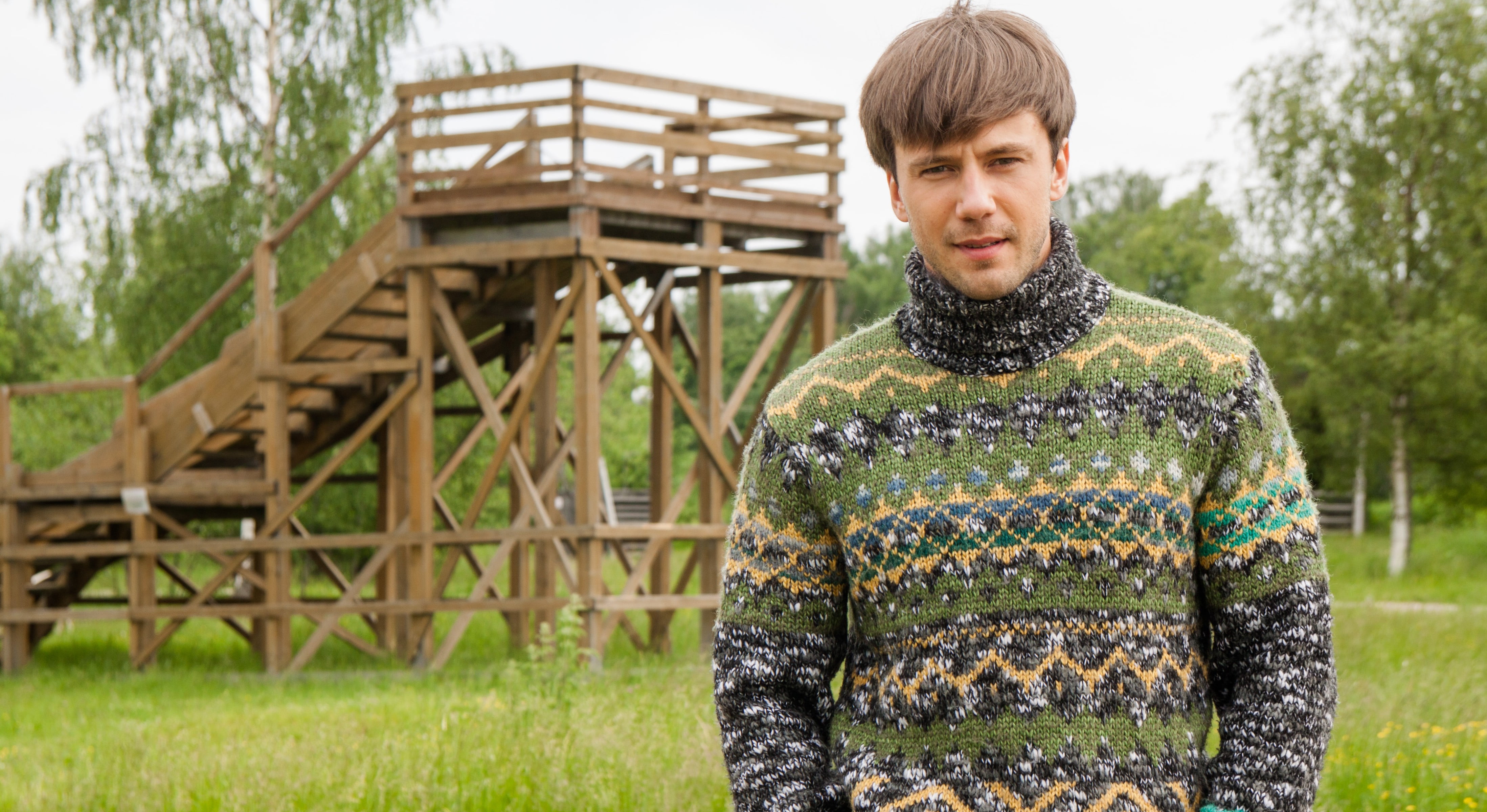 man in green sweater standing behind brown wooden park slide
