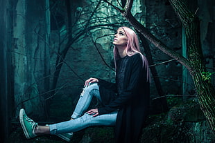 woman wearing black cardigan and blue jeans sitting on tree trunk