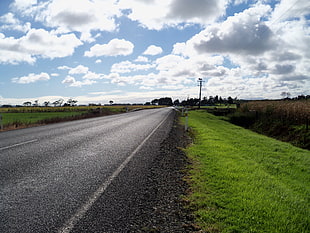 grey asphalt road beside green grass field under cloudy sky