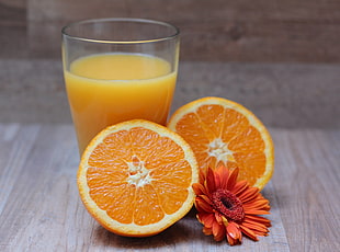 two orange halves, orange gerbera daisy and glass of orange juice