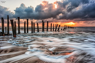 time lapse photography of flowing sea water nearby standing poles HD wallpaper