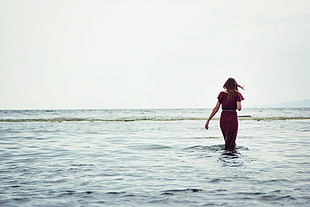 woman in maroon dress walking on seashore during daytime HD wallpaper