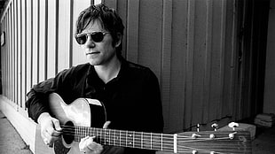man holding brown acoustic guitar and wearing sunglasses