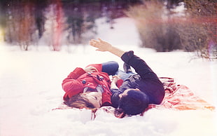 couple in black and red jacket lying on the snow