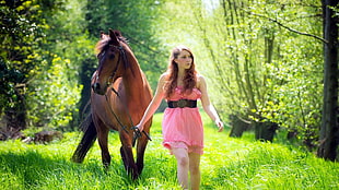 woman wearing pink dress behind brown horse in forest during daytime