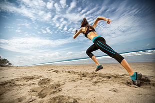 woman in black sports bra and track pants running at beach