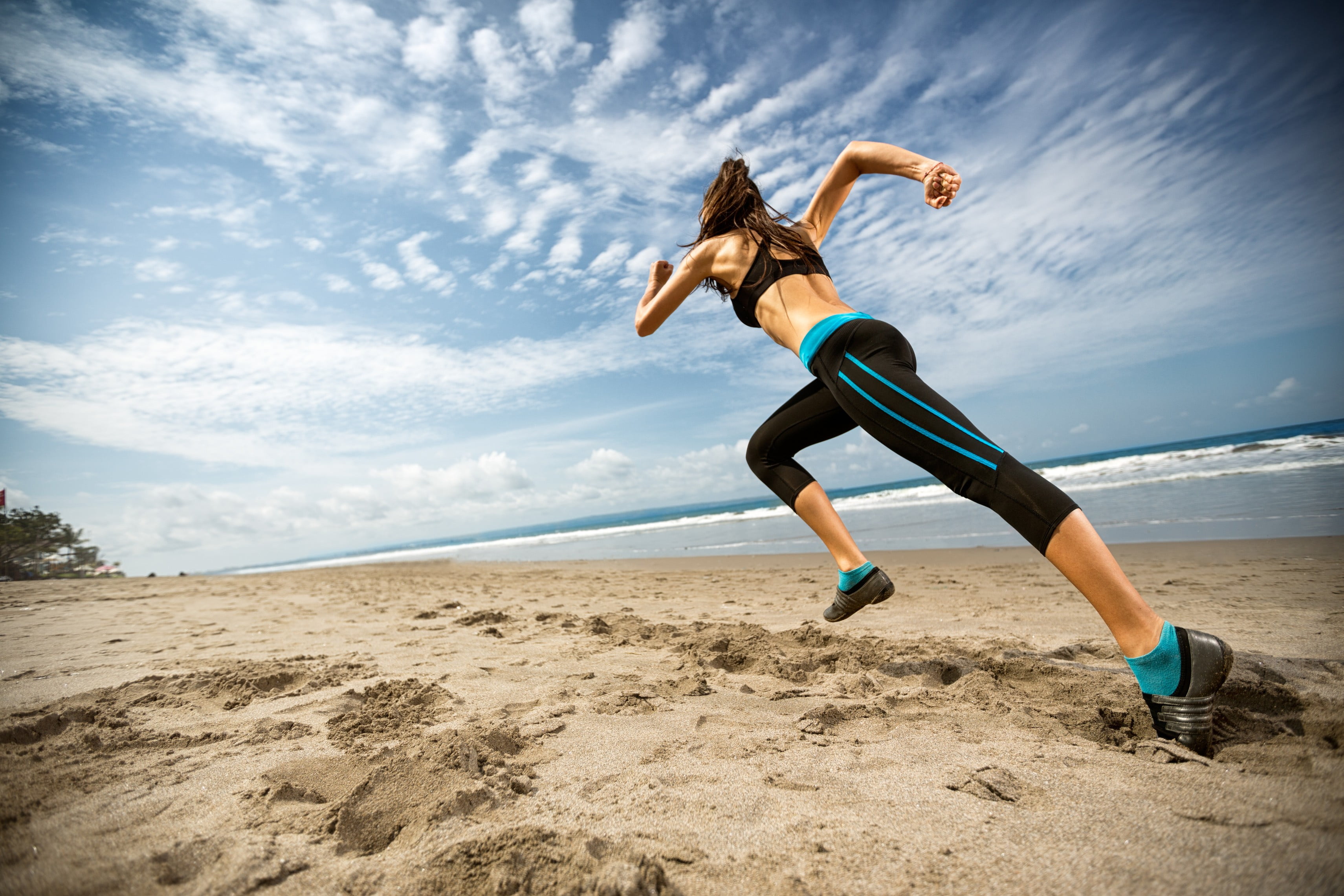 Woman in black sports bra and track pants running at beach HD wallpaper