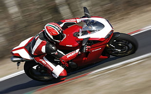 man in black red and white motorcycle suit driving white and black sports motorcycle in race track