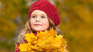 girl wearing red shirt and knit cap holding yellow leaf photography