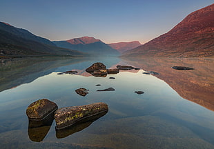 landscape photography of rock on body of water surrounded by mountains, llyn ogwen, snowdonia HD wallpaper