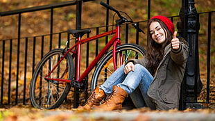 woman in gray coat sitting in front of red bicycle during daytime
